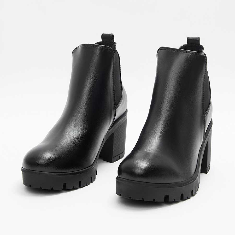 Botines para dama lucy, de color negro. Están fabricados en cuero sintético, son de caña media y tacón medio. Y tienen elásticos en los laterales. Los zapatos están de frente y puestos sobre un fondo blanco.