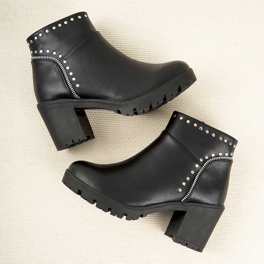 Botines para dama 262, de color negro. Están fabricados en cuero sintético, son de caña baja y tacón medio. Y tienen accesorios plateados como taches y cierre. Los zapatos están de perfil ubicados uno arriba del otro. Todo esto ubicado sobre un tapete  de color beige.