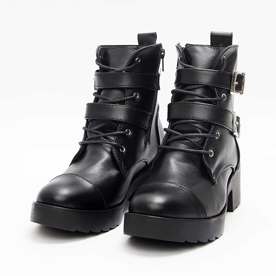 Botines negros para mujer A92. Están fabricados en cuero sintético, son de caña media y tacón bajito. Y tienen accesorios plateados como taches, correas y cierre. Los zapatos están de frente y puestos sobre un fondo blanco.