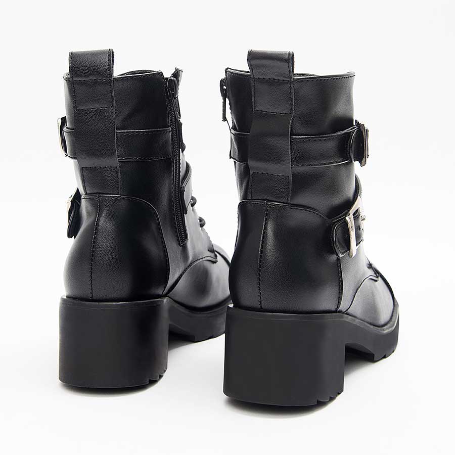 Botines negros para dama A92. Están fabricados en cuero sintético, son de caña media y tacón bajito. Y tienen accesorios plateados como taches, correas y cierre. Los zapatos se ven desde atrás y puestos sobre un fondo blanco.