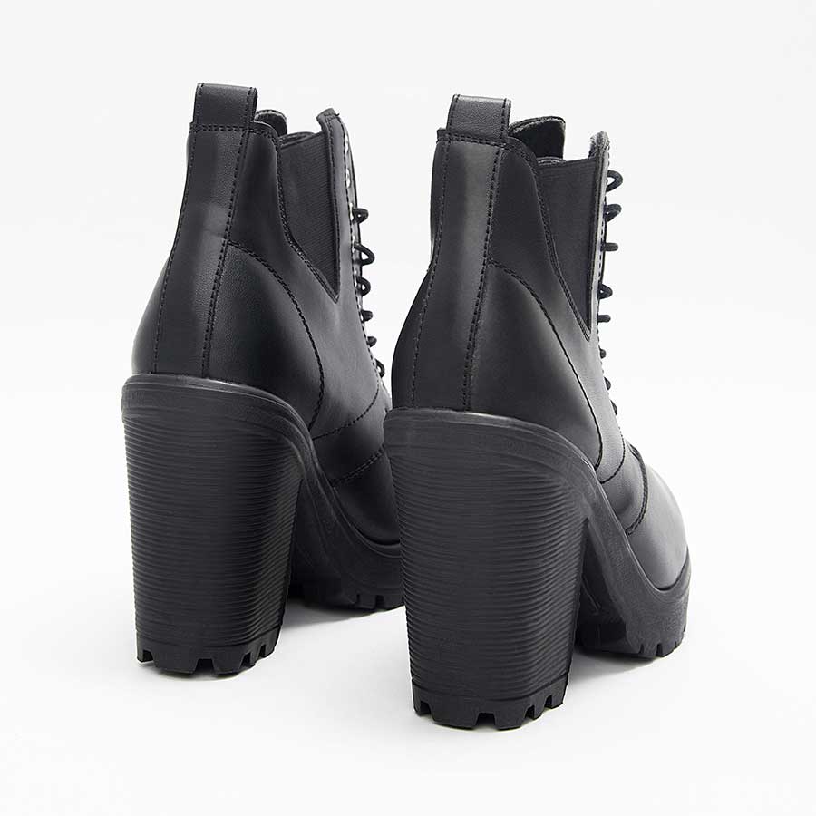 Botines para mujer charlotte, de color negro. Están fabricados en cuero sintético, son de caña media y tacón alto. Y tienen accesorios de cordones y elásticos en los laterales. Los zapatos se ven desde atrás y puestos sobre un fondo blanco.