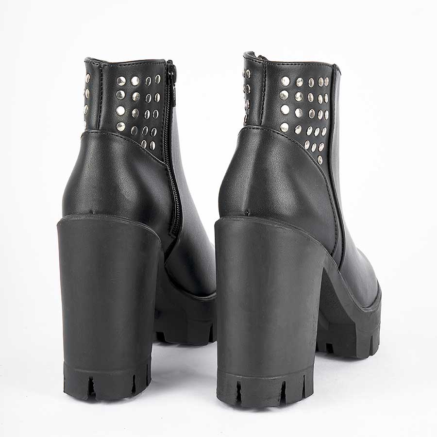 Botines para mujer dominik, de color negro. Están fabricados en cuero sintético, son de caña media y tacón alto. Y tienen accesorios plateados como taches y cierre..Los zapatos se ven desde atrás y puestos sobre un fondo blanco.