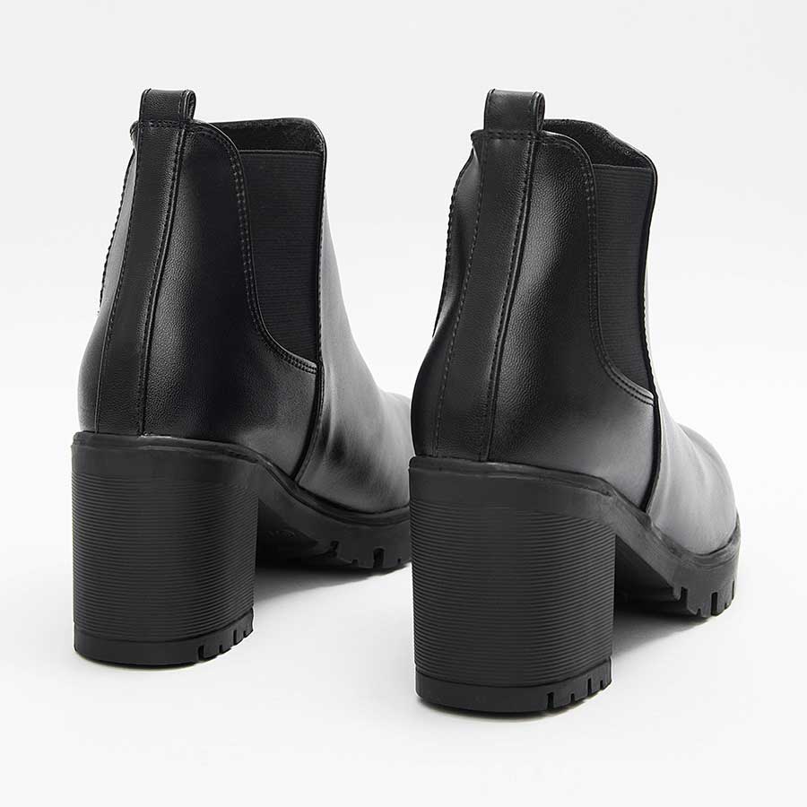 Botines para dama lucy, de color negro. Están fabricados en cuero sintético, son de caña media y tacón medio. Y tienen elásticos en los laterales.Los zapatos se ven desde atrás y puestos sobre un fondo blanco.