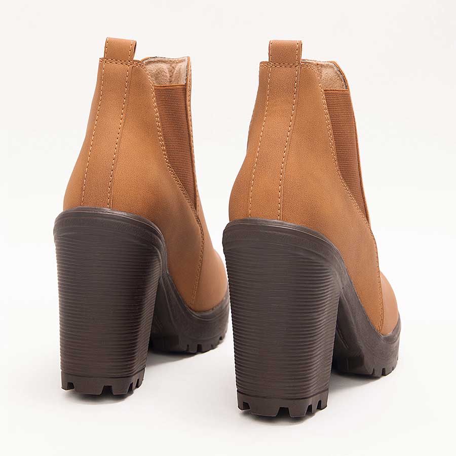 Botines para mujer Sandy, de color miel. Están fabricados en cuero sintético, son de caña media y tacón alto. Y tienen elásticos en los laterales.Los zapatos se ven desde atrás y puestos sobre un fondo blanco.