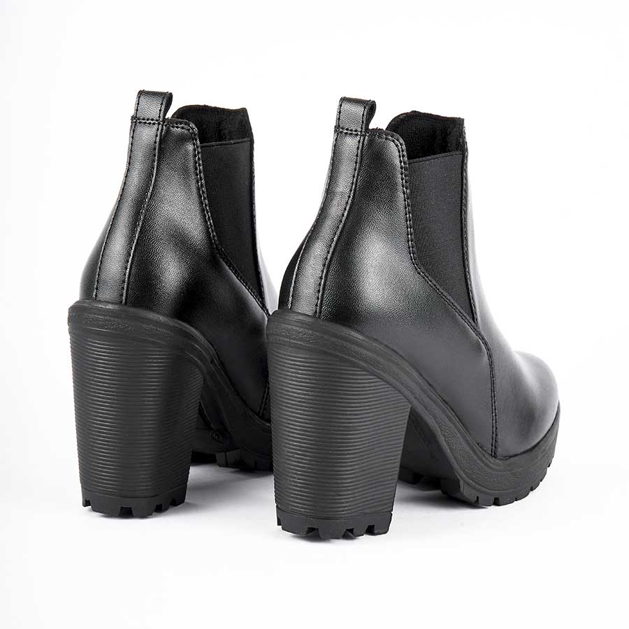 Botines para dama sandy, de color negro. Están fabricados en cuero sintético, son de caña media y tacón alto. Y elásticos en los laterales Los zapatos se ven desde atrás y puestos sobre un fondo blanco.
