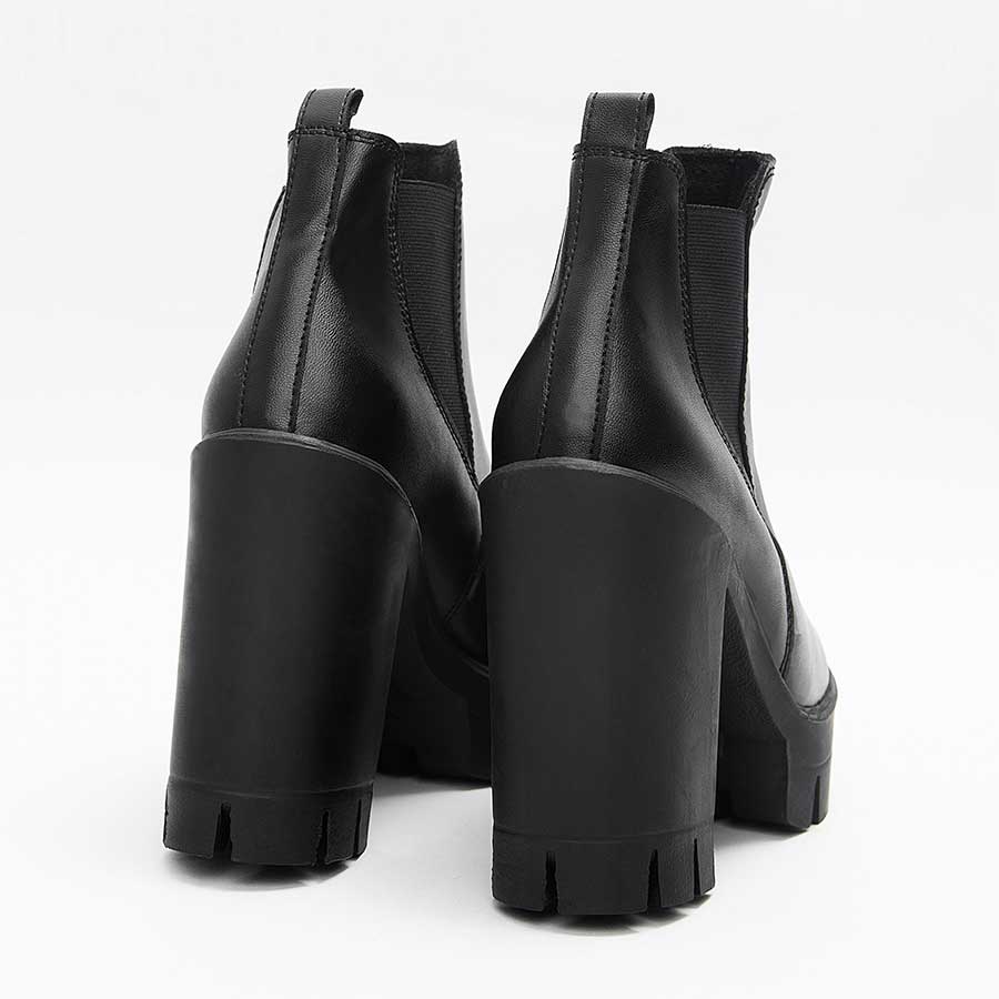 Botines para dama Vegas, de color negro. Están fabricados en cuero sintético, son de caña media y tacón alto. Y tienen elásticos en los laterales. Los zapatos se ven desde atrás y puestos sobre un fondo blanco.