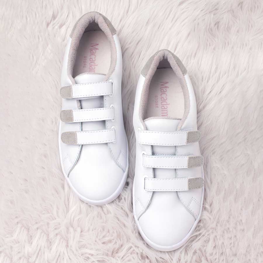 Tenis para dama noa, de color blanco. Están fabricados en cuero sintético, son de plataforma. Y tienen accesorios plateados, cierres y cordones. Los zapatos están de  frente uno al lado del otro. Todo esto ubicado sobre un tapete peludo de color blanco.