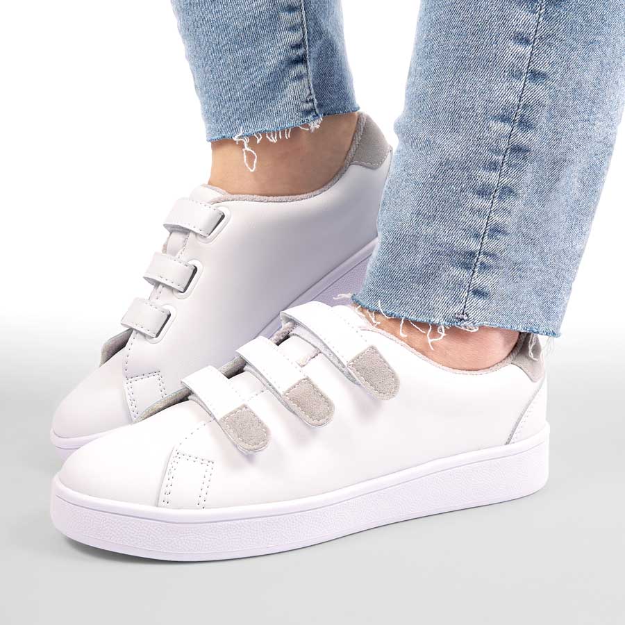 Tenis para dama Noa, de color blanco. Están fabricados en cuero sintético, son de plataforma Y tienen accesorios como correas. Los zapatos los lleva calzados una modelo que lleva puestos unos jeans y está parada sobre un fondo claro.