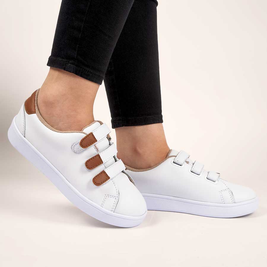 Tenis para dama Noa, de color blanco. Están fabricados en cuero sintético, son de plataforma Y tienen accesorios como correas. Los zapatos los lleva calzados una modelo que lleva puestos unos jeans y está parada sobre un fondo claro.